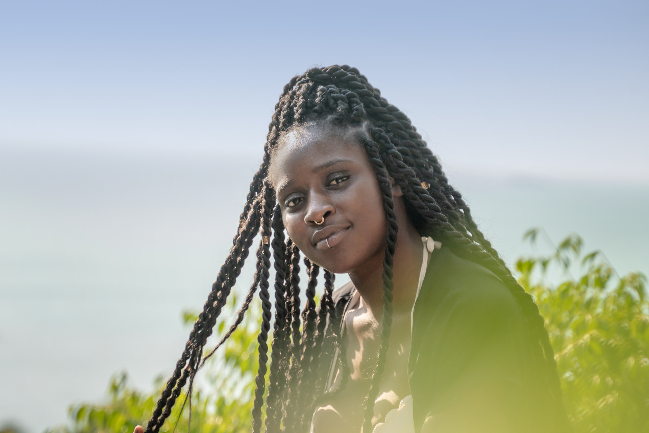 Charming beautiful young african american woman girl with black pigtails with piercings on her face against the background of the sea.