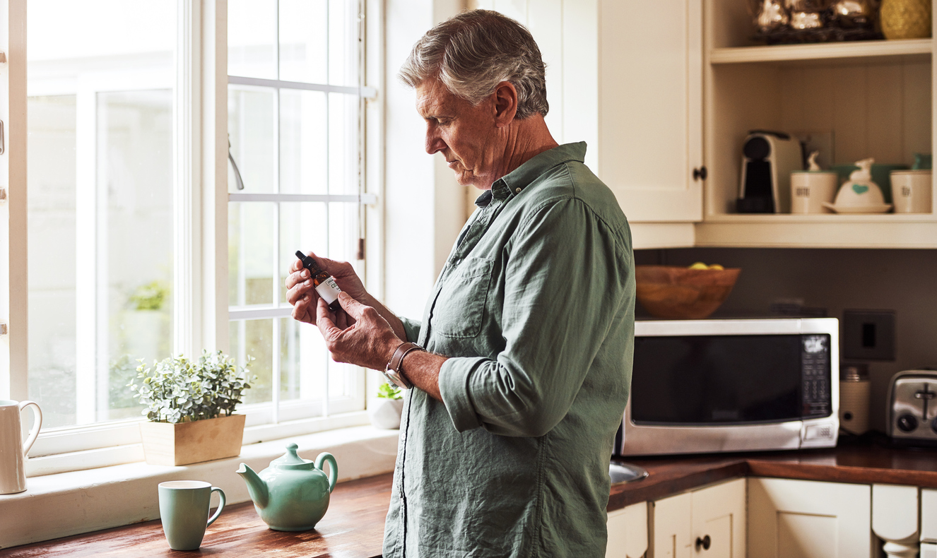 A man holding a CBD oil bottle reading the label in a kitchen